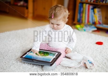 Cute Adorable Baby Girl Watching Cartoons On Tablet Pc. Todder Child At Home Touching On Screen And 