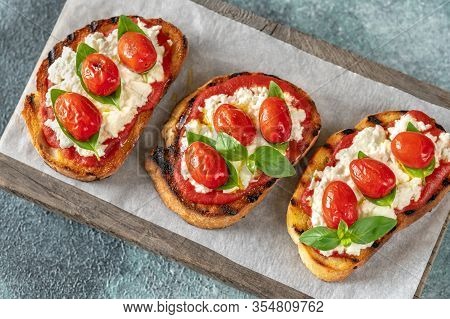Italian Bruschettas With Mozzarella, Riccotta, Baked Tomatoes And Basil