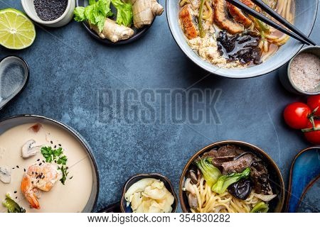 Set Of Serving Asian Soups On Dark Blue Background Top View. Tom Yum Soup, Eel Fish Soup And Ramen N