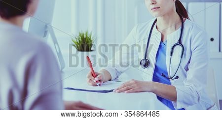 Doctor and patient discussing medical problems in a hospital consulting room. Doc filling in a patient's form