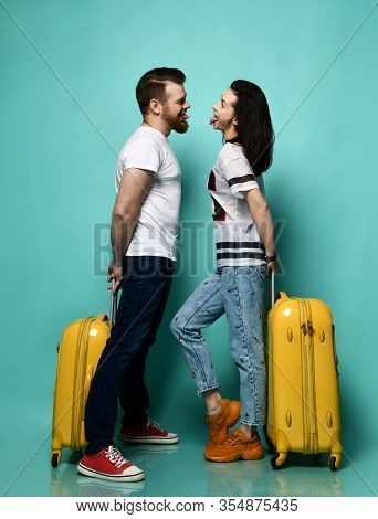Male And Female In Casual Clothes Are Showing Tongues To Each Other, Posing With Yellow Suitcases, S