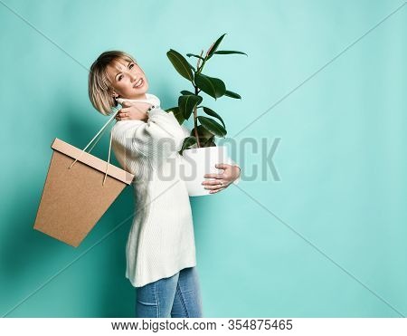 Attractive Blonde Female In White Sweater, Jeans And Bracelet. She Is Smiling, Holding Paper Bag And