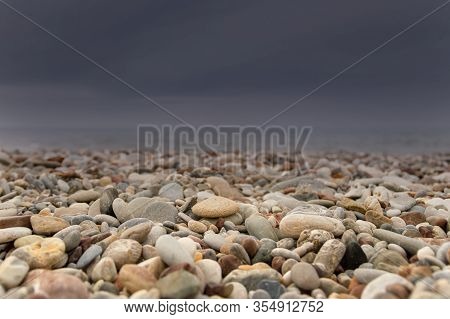 Strong Storm Is Approaching From The Sea On The Shingle Beach. Dark Storm Clouds And Sunlit Pebbles