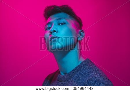 Portrait Of A Guy With Colorful Neon Light On Pink Studio Background. Male Model With Calm And Serio