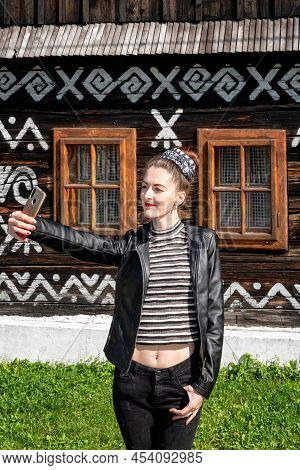 Young Pretty Girl Dress In Black Making A Selfie Photo In Front Of Old Cottage In Rural Village Cicm