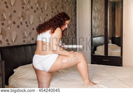 Curly Plus Size Woman In White Underwear Stand Near Bed In Bedroom And Wrap Hip With Cling Film Back