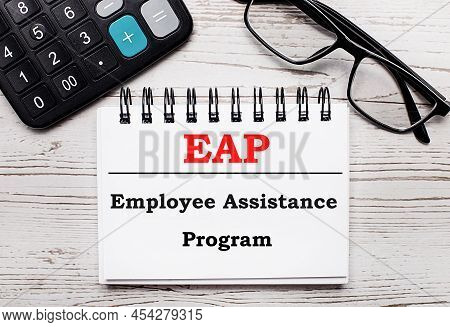 On A Light Wooden Table Calculator, Glasses And A Blank Notepad With The Text Eap Employee Assistanc