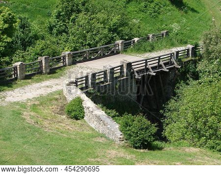 An Ancient Bridge, A Concrete Bridge Among Two Hills And Green Grass, Thickets. Beautiful Nature Bac