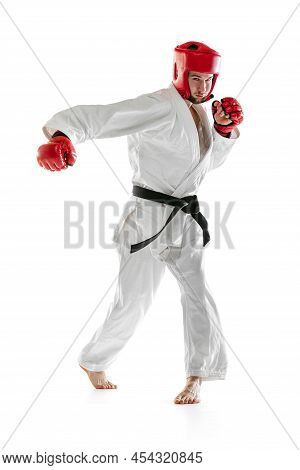 Portrait Of Young Sportive Man Wearing White Dobok, Helmet And Gloves Practicing Isolated Over White