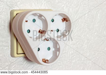 White Three-pronged Socket Adapter With Grounding In The Room Wall Front View