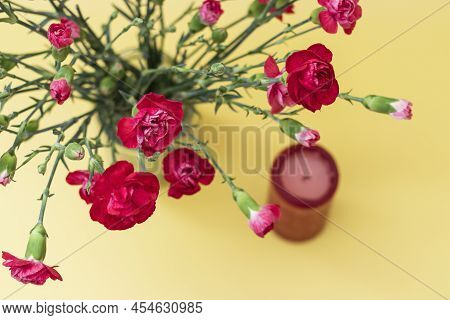 Red Mini Carnation Flowers On Yellow Background. Next To A Red Andle, The Concept Of Relaxation For 