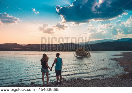 Young Attractive Couple Holding Hands In A Beautiful Lake In Summer During Sunset. Discovery Travel 