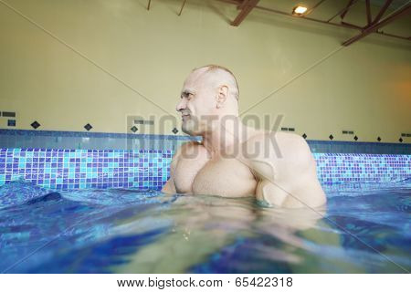 Wet bodybuilder looks away in pure water of swimming pool of gym hall