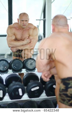 Middleaged bodybuilder in shorts looks into mirror at his muscles 