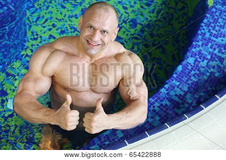 Top view of happy bodybuilder showing thumbs-up gesture in swimming pool 