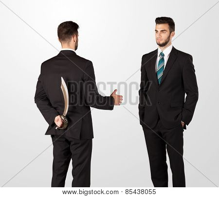 Two opposing businessman shake hands, one of them hiding a weapon behind his back