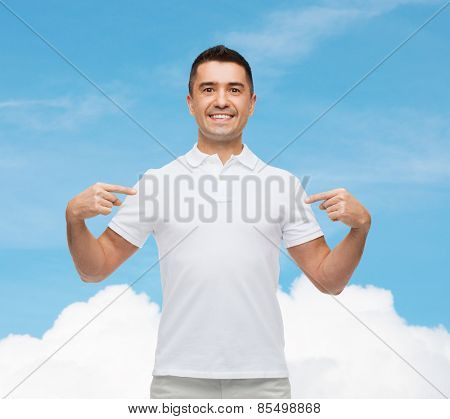 happiness, advertisement, fashion, gesture and people concept - smiling man in t-shirt pointing fingers on himself over blue sky and cloud background