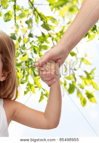 people, charity, family and adoption concept - close up of woman and little girl holding hands over green tree leavers background