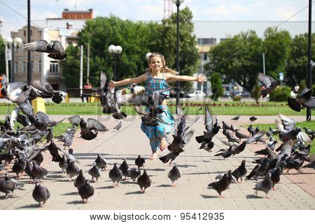 Young happy girl runs through a flock of pigeons on the square in summer city park