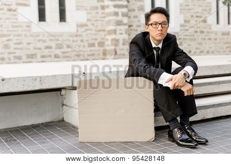 Businessman in a city street sitting next to blank banner