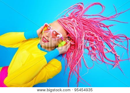 Ultra trendy DJ party girl in bright clothes, headphones and with bright dreadlocks. Disco, party. Show business. Bright fashion.