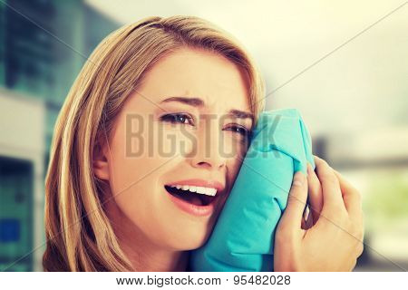 Woman having tooth ache holding ice bag near face