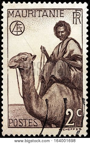 LUGA RUSSIA - NOVEMBER 29 2016: A stamp printed by MAURITANIA shows Nomand Man on Dromedary against native desert landscape circa 1938