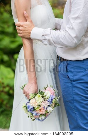 Wedding: beautiful young bride and groom standing in a park outdoors holding hands and smiling