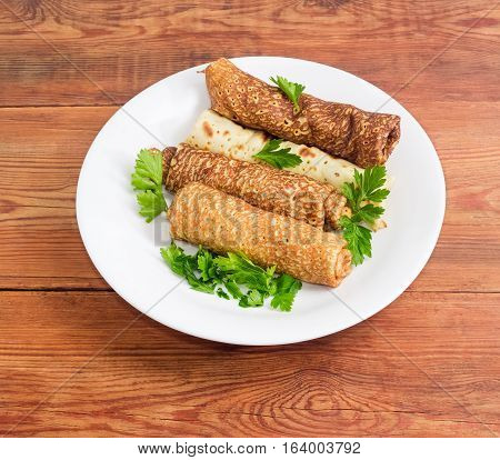 Pancakes filled with meat filling and parsley twigs on a white dish on an old wooden surface