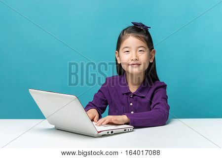 Cute Asia Little Girl Who Enjoy The Laptop Computer On Blue Background