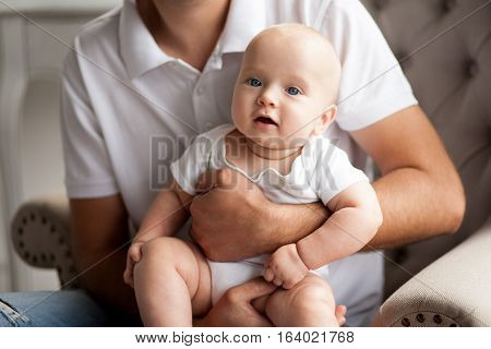 Portrait of small baby. Child sits on hands at the daddy.