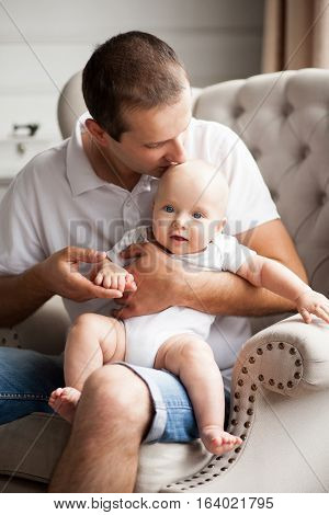 Small baby with his father. Father sits and holds baby in his hands.