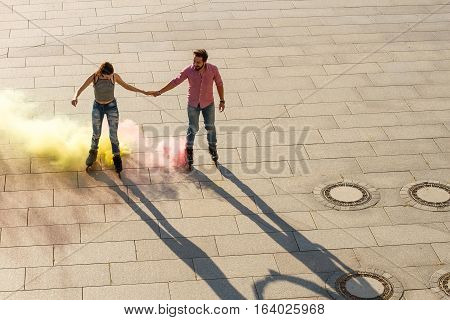 Couple rollerskating in the street. Bright smoke coming from rollerskates. We will colorize the world.