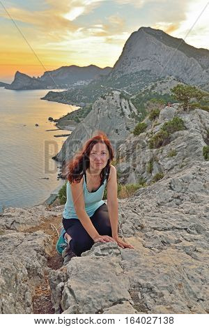 The girl sits on a high hill by the sea at sunset. Sudak. Crimea