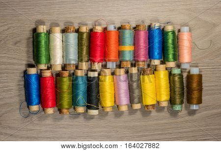 Sewing thread reels on a wood textured background. Bobbins of thread lined up in a row.