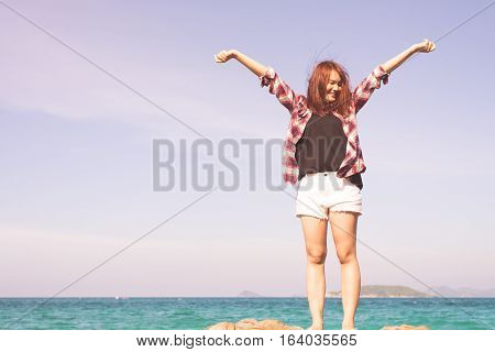 Woman relaxing at beach enjoying summer freedom with open arms and hair in the wind by the water seaside. Asian girl on summer travel holidays vacation outside. Vintage effect style pictures.