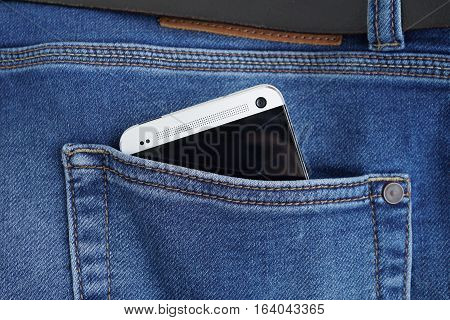 Silver aluminum smartphone placed at the male stitched blue jean's backpocket