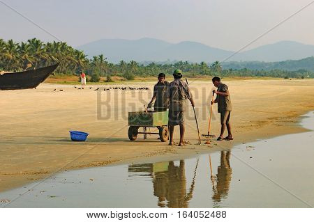 Goa, India - November 23, 2012: A team of workers begin clearing the Cavelossim Beach from plastic bottles and other trash South Goa India.