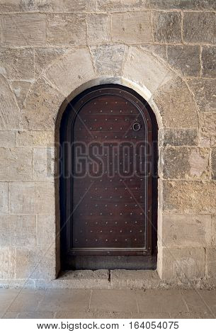 Wooden aged vaulted ornate door and stone wall at caravansary (Wikala) of Bazaraa, Medieval Cairo, Egypt