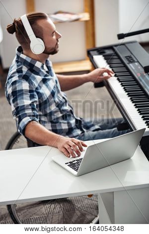 Feeling the vibe. Brilliant concentrated disabled musician editing recently recorded material creating a new song while sitting at the piano and using his laptop