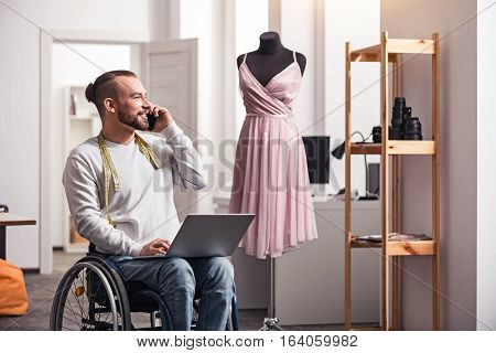 You should come around. Delighted handsome enthusiastic designer talking on the phone with his friend and seeking advice on creative decisions while working in his home studio