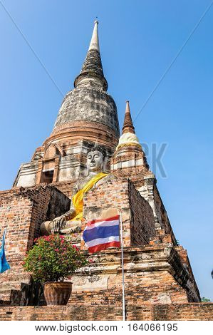 Buddha statue at the bottom of a large ancient pagoda on blue sky background at Wat Yai Chai Mongkon temple in Phra Nakhon Si Ayutthaya Historical Park Ayutthaya Province Thailand