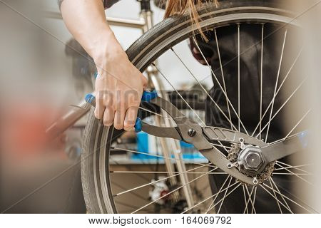 Skillful craftswoman working. Strong athletic masterful craftswoman standing in the workshop and working while fixing the chain of the bicycle and holding different tools