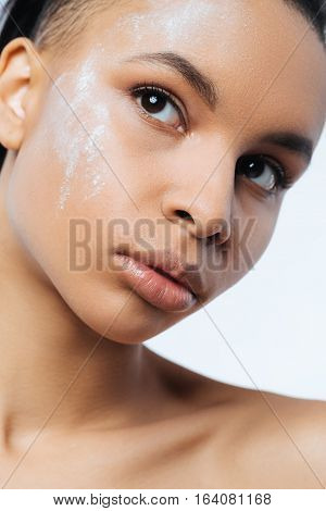 White powder. Pleasant nice woman standing against the white background and looking somewhere up while having white powder on her face