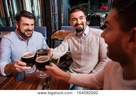 Male company. Delighted positive nice man drinking beer and chatting with each other while meeting in the pub