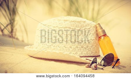 Summer vacations concept. Beach accessories. Straw hat sunglasses and sun oil on sand.