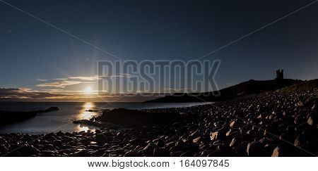 Hunters super moon rising in the night sky over Dunstanburgh Castle Northumberland UK