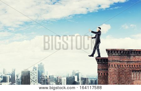 Businessman with blindfolder on eyes walking on building top
