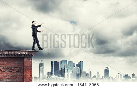 Businessman with blindfolder on eyes walking on building top