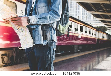 Backpacker Waiting For Long Journey Travel At Train Station With Backpack And Map On Hand. Travel Co